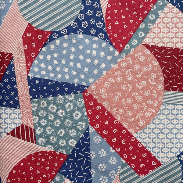 Quilt pattern with red, blue, and pink geometric shapes on a fabric background